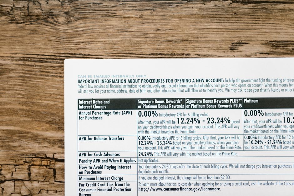 A close-up photograph of a printed document placed on a wooden surface. The page contains financial information including interest rates, APR percentages, and other related text, with headings and tables in black and blue ink. The document is partially visible, showing the top part of the page, with the edges aligned parallel to the wooden grain. The background consists of a natural, textured wooden surface with wood grain patterns. The image appears to be captured during a house relocation or packing process, with the document possibly being part of moving paperwork or packing materials involved in a home or office removal service, as offered by Removal Van Lambeth. No furniture, boxes, or moving equipment are visible in this image, focusing solely on the paper and wooden surface.